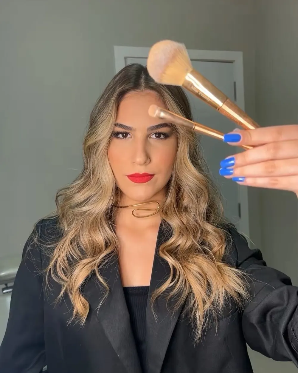 Laura Silveira, maquiadora, de batom vermelho e pincel na mão