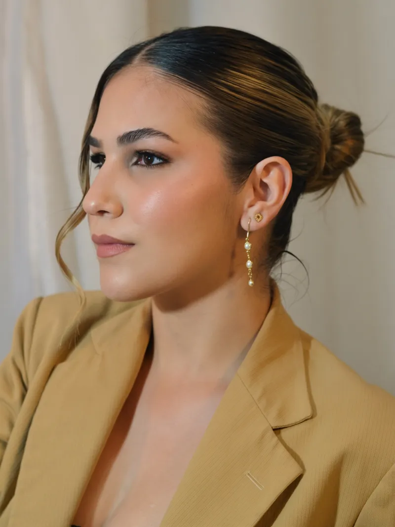 Laura Silveira de perfil, com coque baixo, brincos de pérola e blazer caramelo