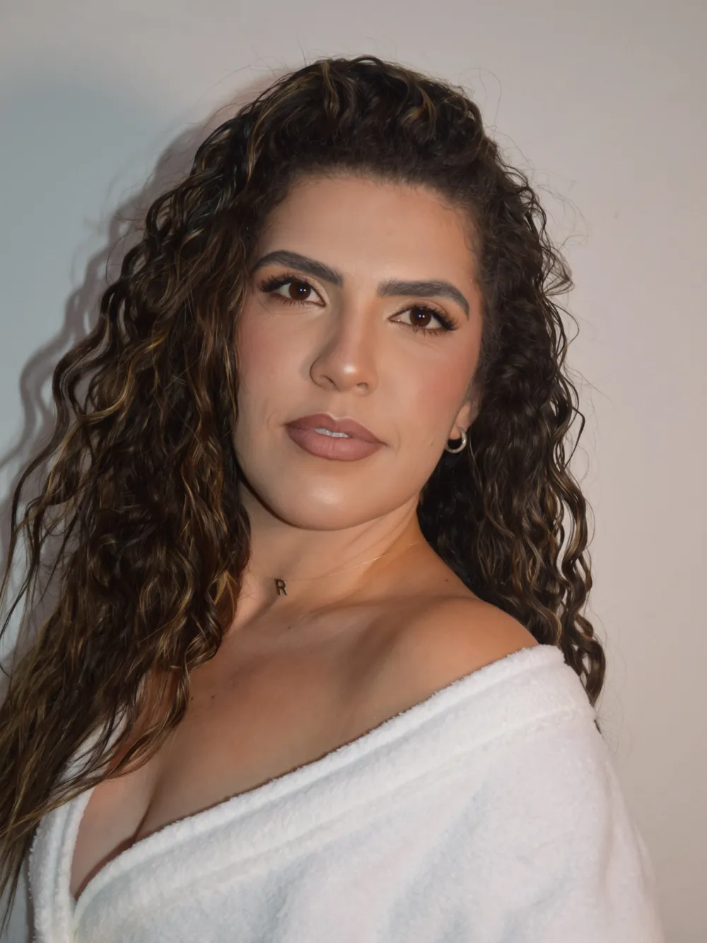 Cliente de cabelo cacheado com pele natural, olhar esfumado e boca nude
